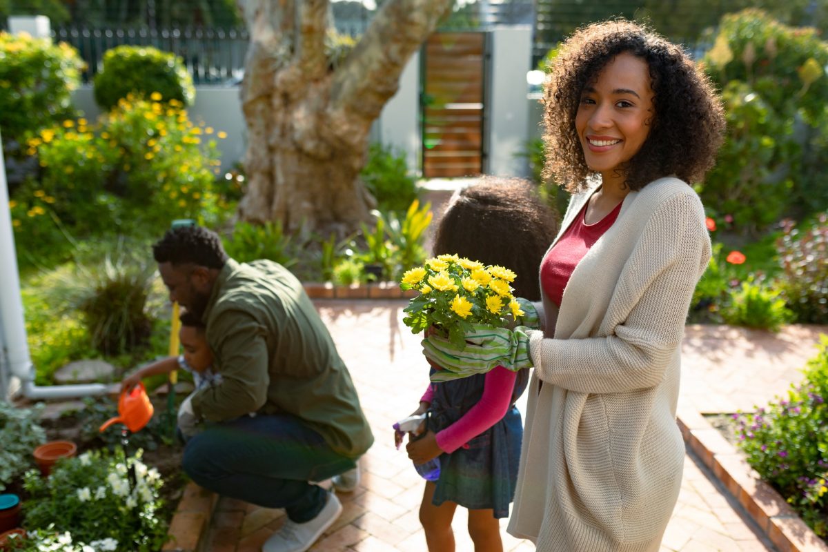 Happy african american mother holding flowers, gardening with children and husband