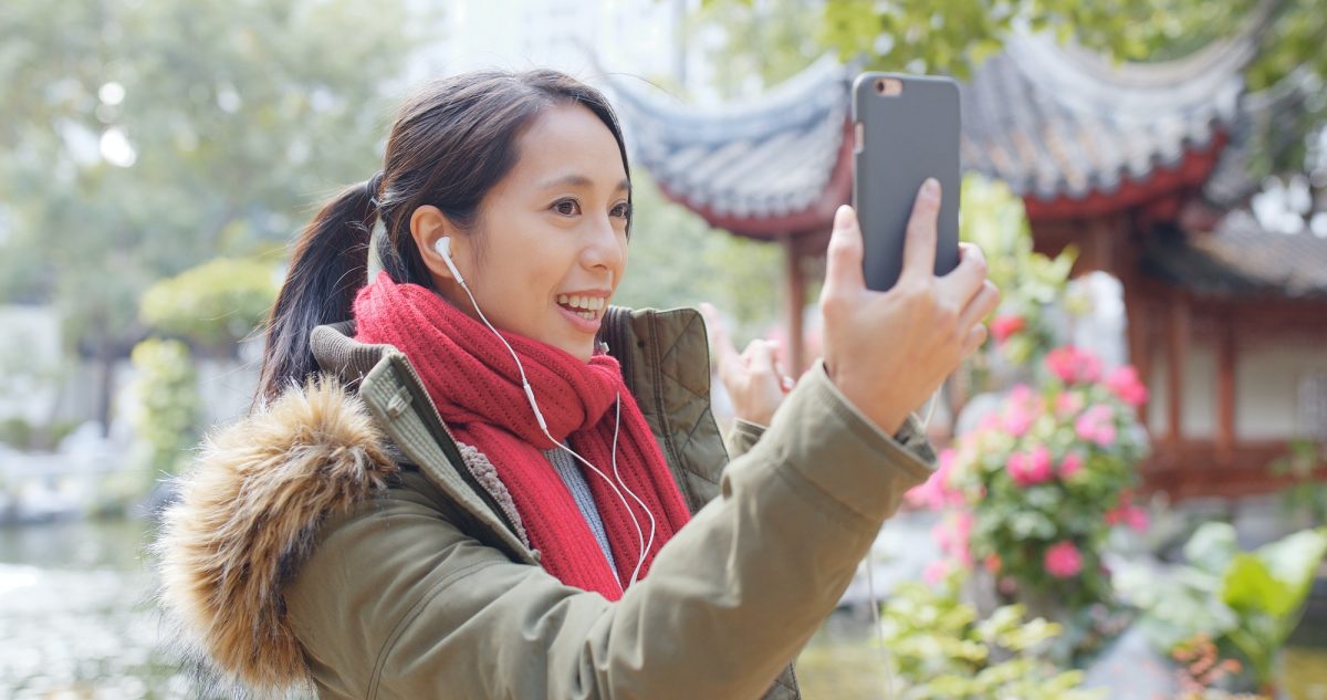 Woman making live stream on cellphone in chinese garden